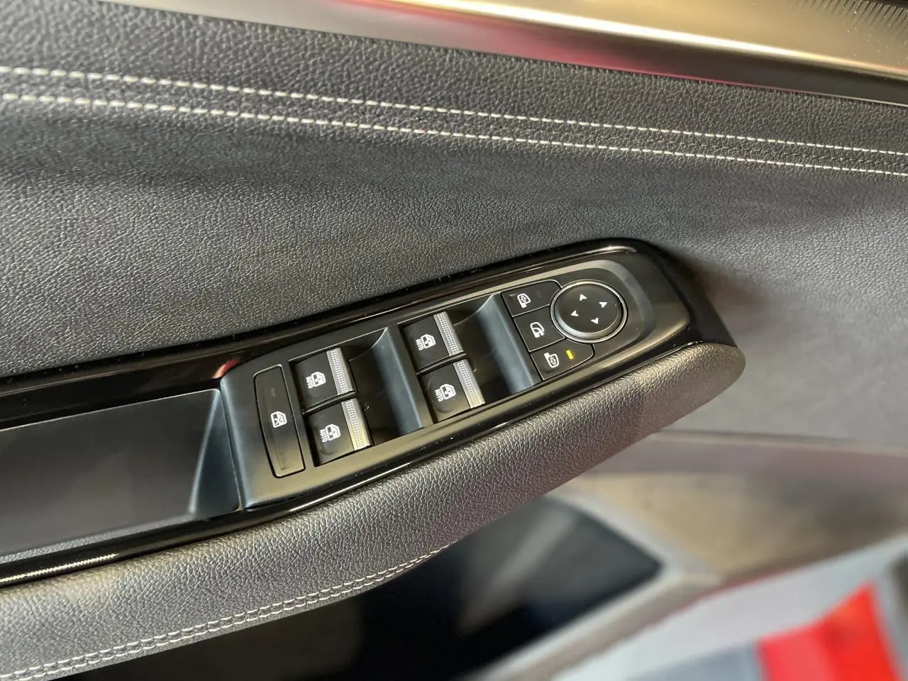 Détail des commandes de lève-vitres sur la porte côté conducteur d’un Renault Rafale rouge avec surpiqûres argentées.
