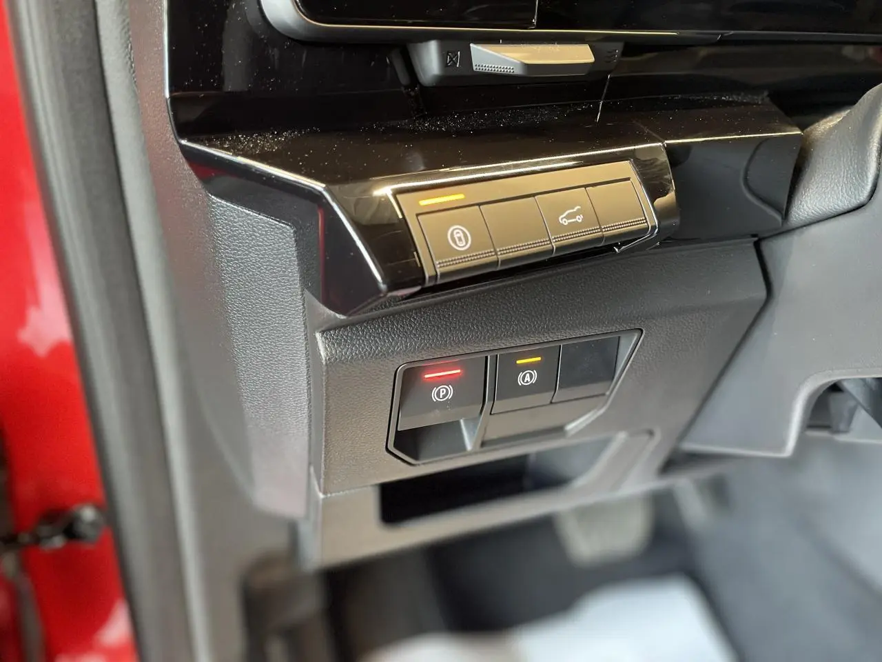 Gros plan sur les commandes de la console côté conducteur, avec partie de la portière rouge visible en arrière-plan.