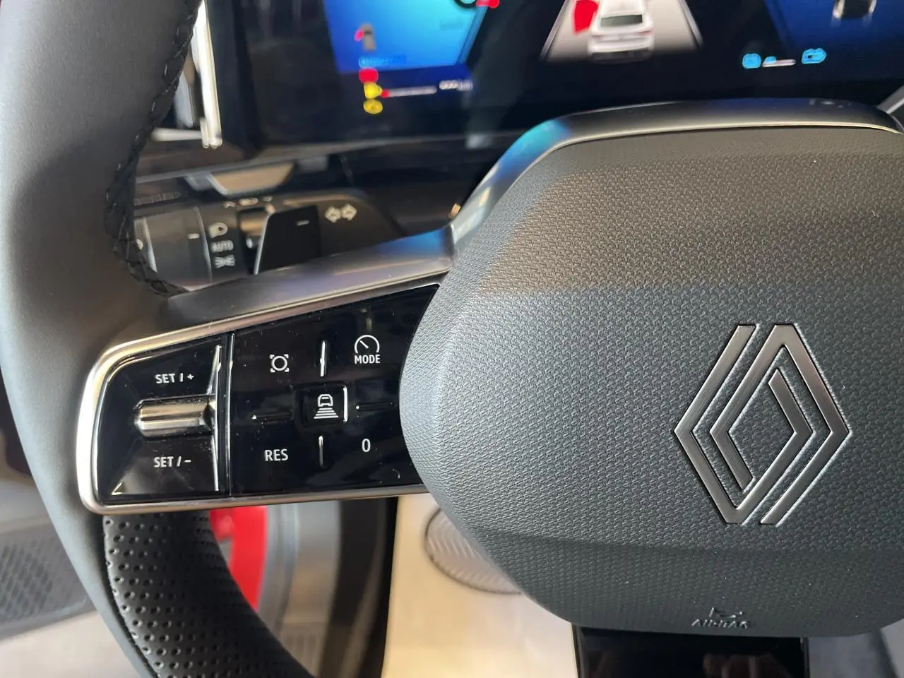 Gros plan sur le volant noir texturé de la Renault Rafale 2025 avec commandes intégrées et logo Renault argenté.