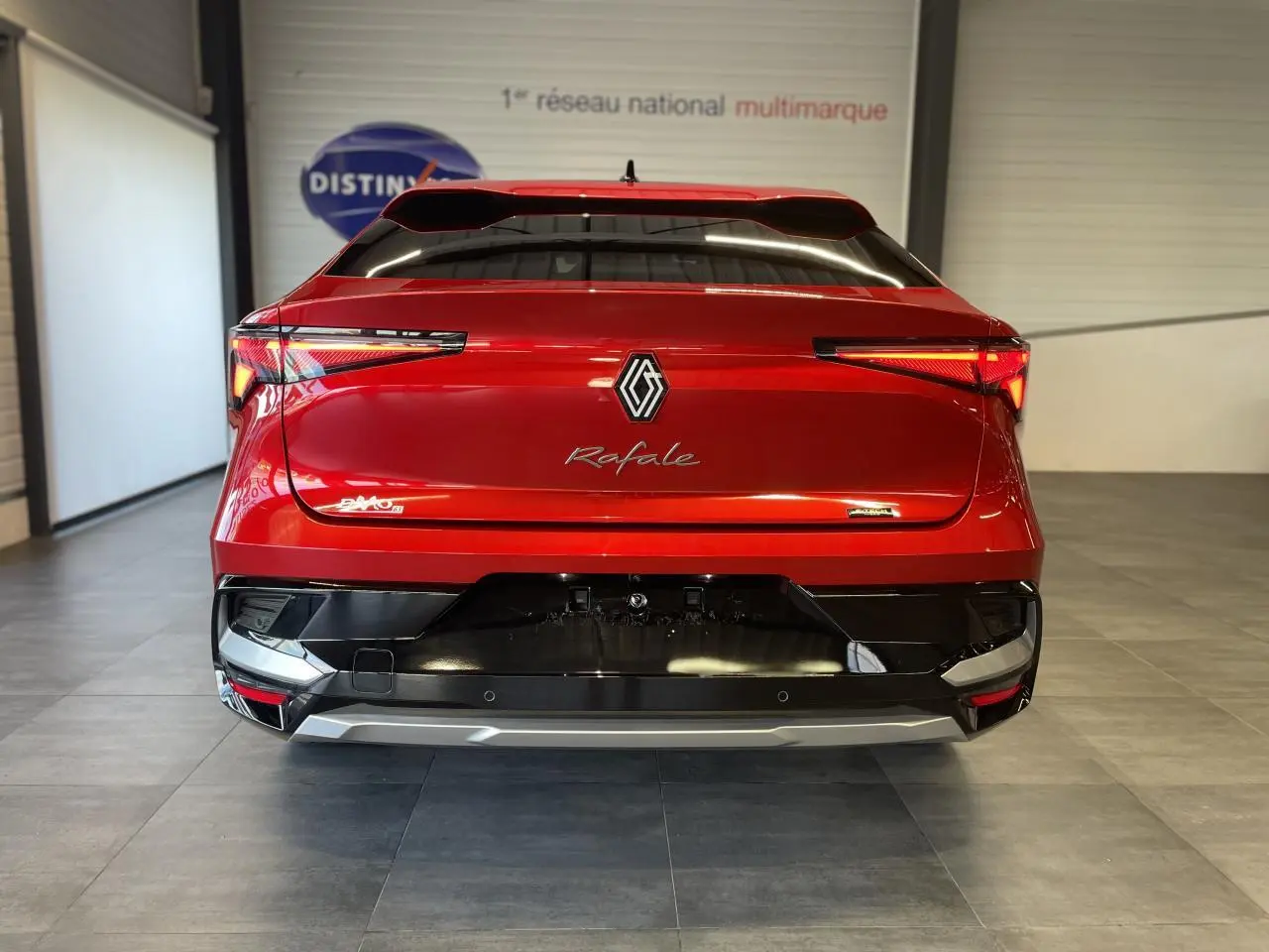 Vue arrière d'une Renault Rafale rouge à toit noir, avec feux LED fins et logo central dans un showroom.