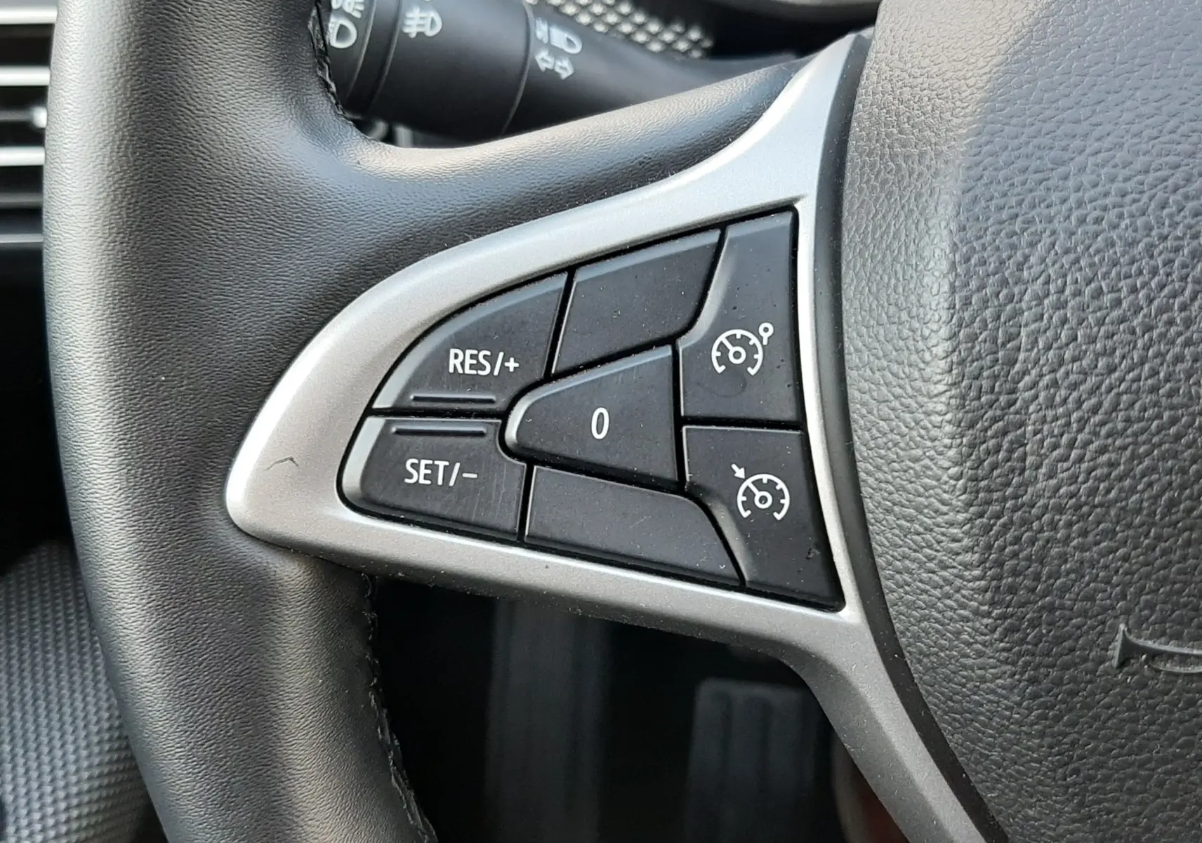Gros plan sur les commandes de régulateur de vitesse à gauche du volant noir du Dacia Jogger 2025.