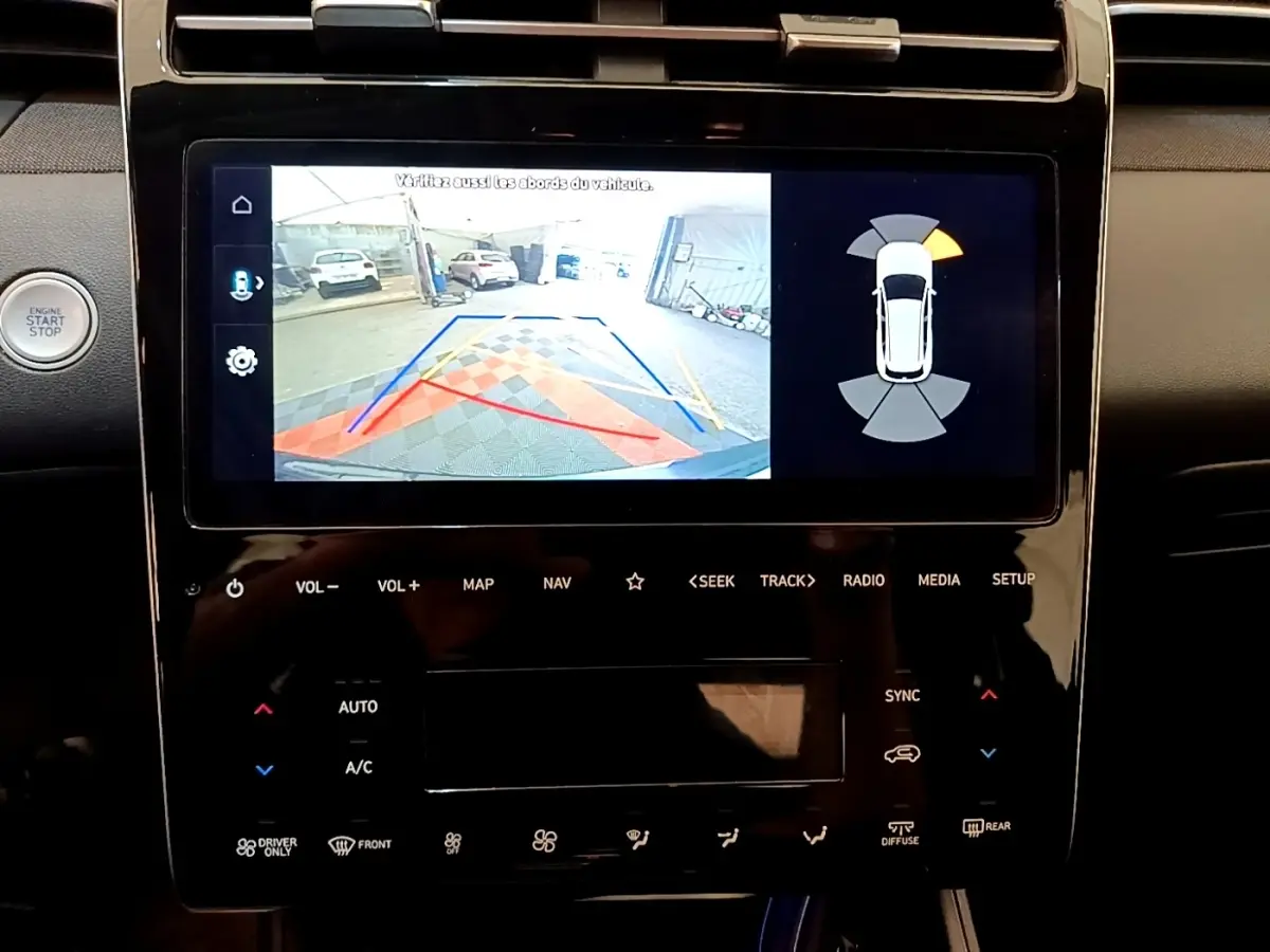 Vue rapprochée de l’écran tactile central du Hyundai Tucson gris foncé 1.6 Hybrid 230 Creative avec affichage caméra de recul et radar.