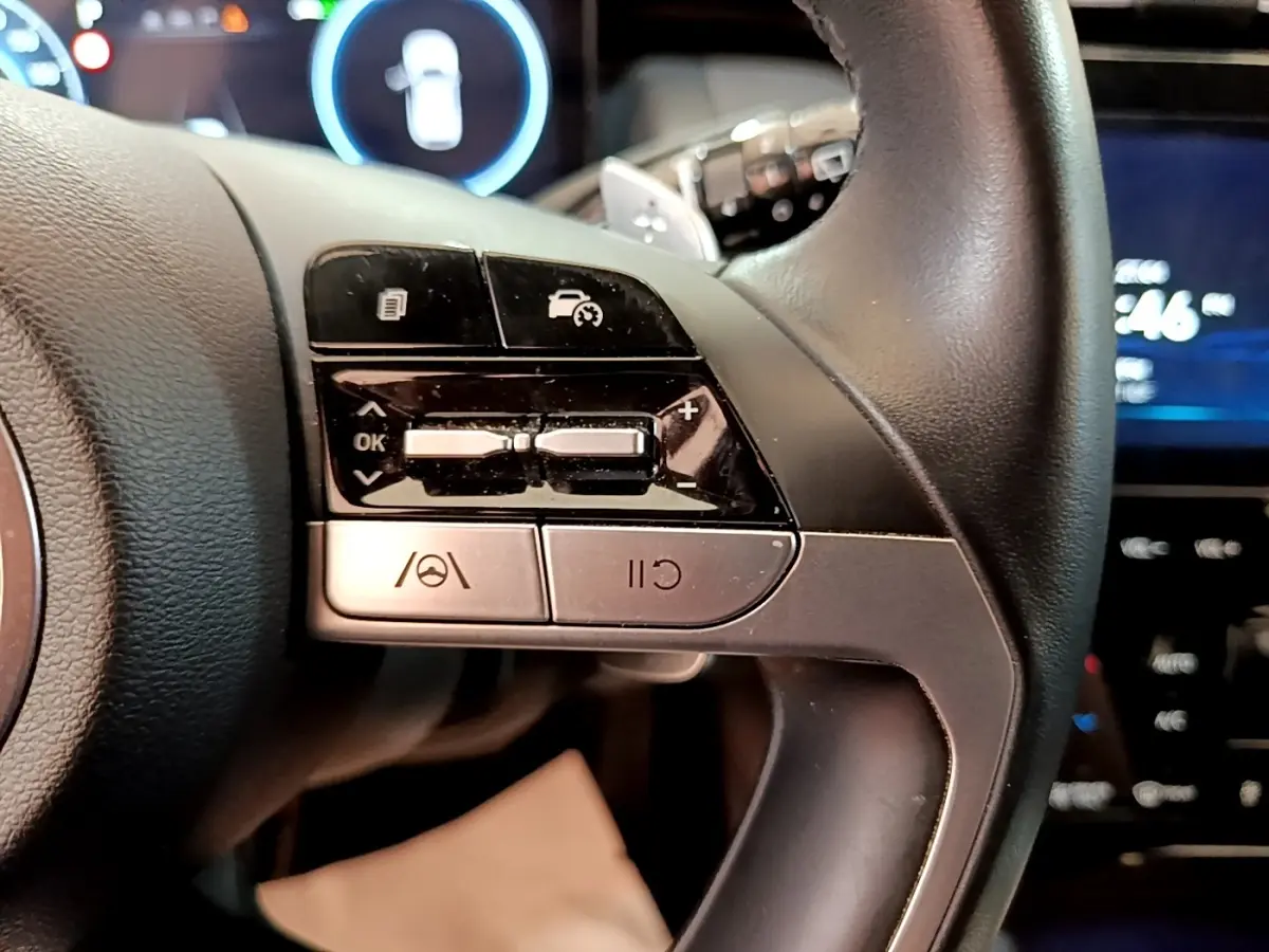 Gros plan sur le volant cuir noir du Hyundai Tucson 1.6 Hybrid 2022, avec commandes multifonctions et affichage digital en arrière-plan.