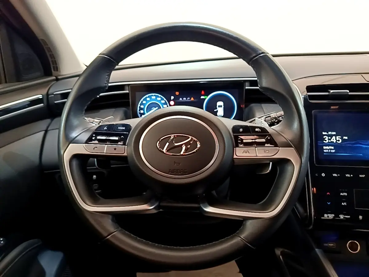 Vue frontale du volant en cuir noir du Hyundai Tucson 1.6 Hybrid 230 avec tableau de bord numérique et écran tactile central.