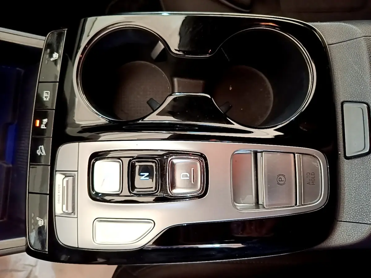 Gros plan sur la console centrale noire et argentée du Hyundai Tucson 1.6 Hybrid 230, avec commandes de boîte auto et porte-gobelets.