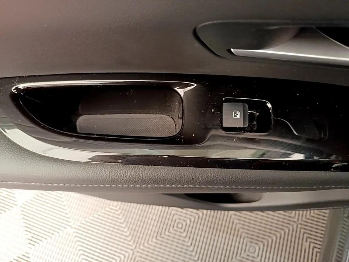 Gros plan sur la poignée intérieure noire de la porte avant droite du Hyundai Tucson gris foncé, bouton de verrouillage visible.