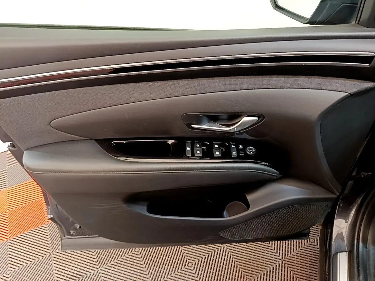 Vue intérieure côté gauche de la porte avant d’un Hyundai Tucson gris foncé, avec commandes de vitres et poignée argentée.