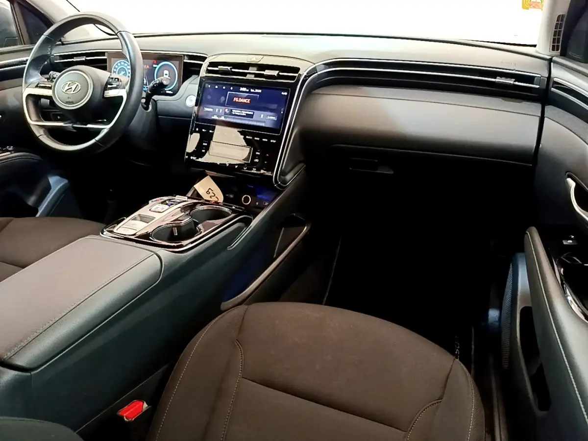 Intérieur du Hyundai Tucson 1.6 Hybrid 230, vue côté passager, tableau de bord noir avec écran tactile central lumineux.