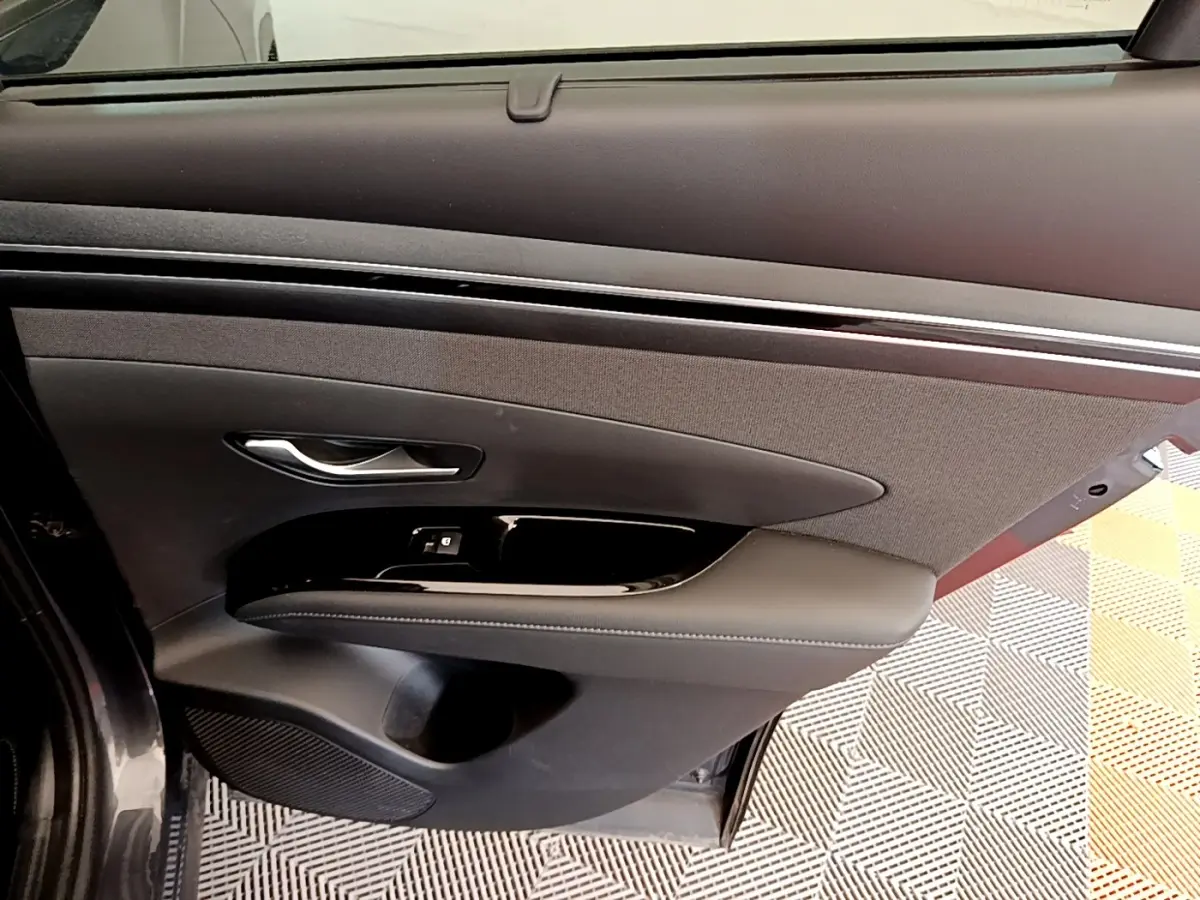 Vue rapprochée de la porte avant gauche gris foncé du Hyundai Tucson 1.6 Hybrid 230 Creative avec garniture noire et poignée argentée.