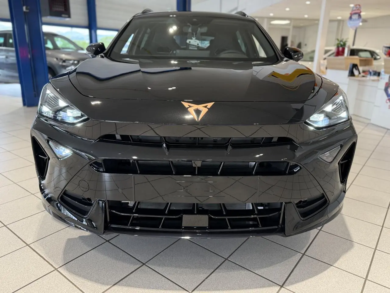 Vue frontale d'un CUPRA Formentor noir Night avec logo cuivré et phares LED allumés en showroom.