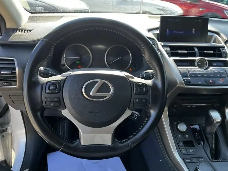 Vue intérieure centrée sur le volant cuir noir du Lexus NX 300H blanc nacré, avec tableau de bord et écran multimédia visibles.