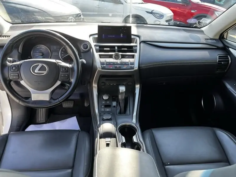 Vue intérieure avant de la Lexus NX 300H blanc nacré, tableau de bord avec écran central et volant cuir noir.