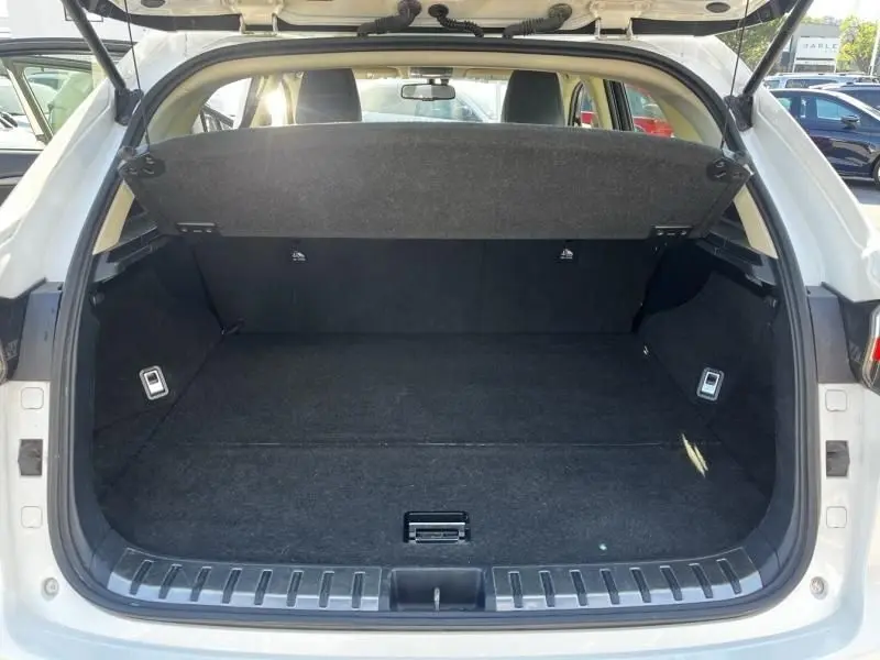 Coffre ouvert vu de l’arrière d’un Lexus NX 300H blanc nacré, montrant un espace de chargement vide et propre.