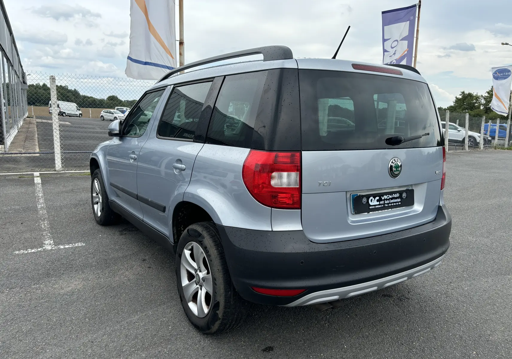 Vue 3/4 arrière droite d'un Skoda Yeti gris 2012 avec jantes alliage et toit équipé de barres de toit.
