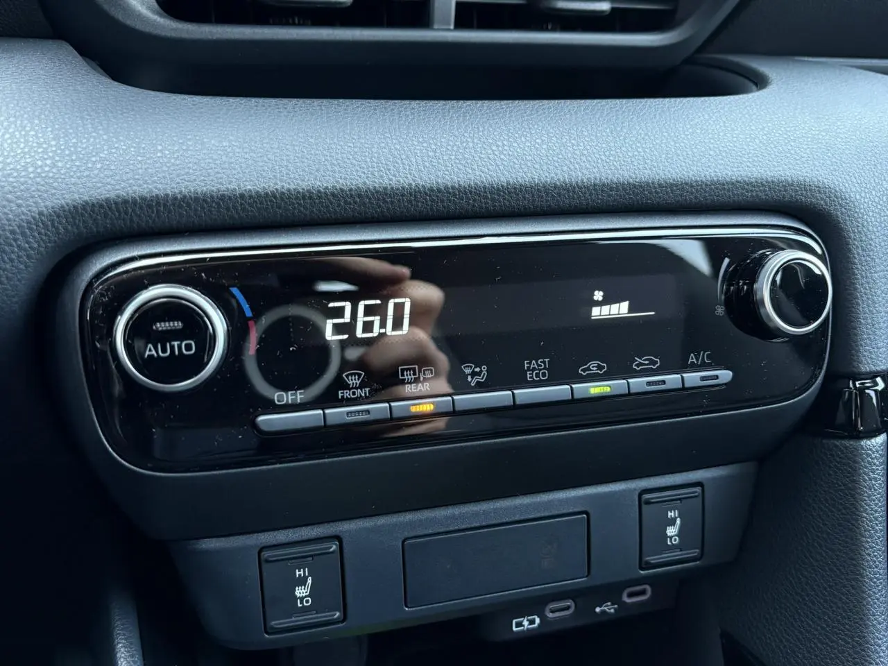 Gros plan sur la console centrale noire de la Toyota Yaris 2025, affichant la climatisation automatique à 26°C et les sièges chauffants.