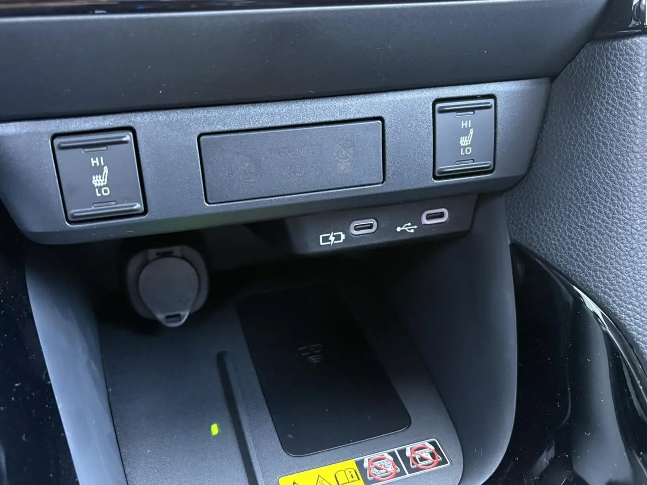 Vue rapprochée de la console centrale de la Toyota Yaris 2025 noire, montrant les commandes des sièges chauffants et le chargeur à induction.