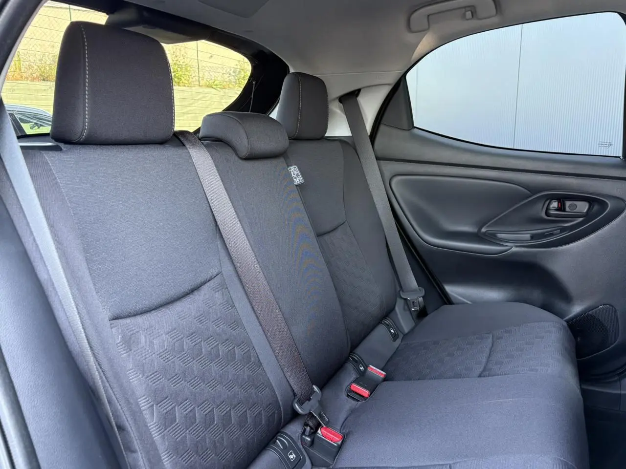 Vue côté droit des sièges arrière en tissu gris foncé de la Toyota Yaris Hybride 2025 avec ceinture de sécurité et porte intérieur noir.