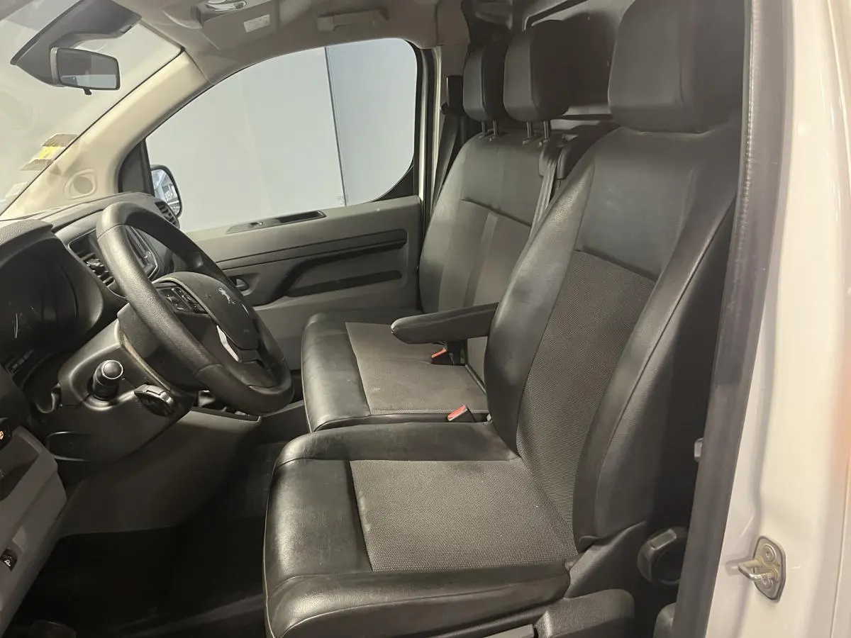 Vue intérieure côté conducteur du Peugeot Expert Fourgon blanc 2020, sièges en tissu et cuir noir avec accoudoir.