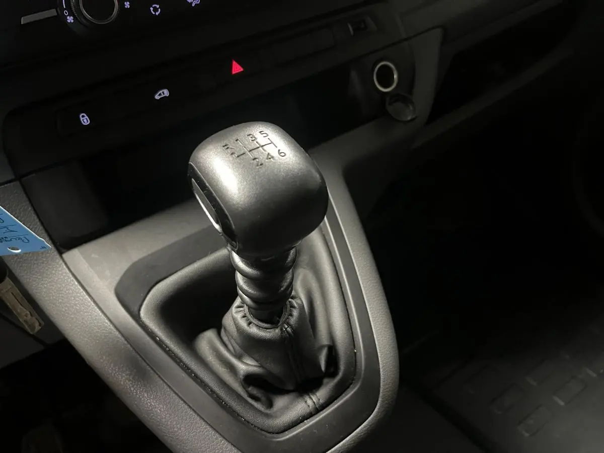 Gros plan sur le levier de vitesses manuel noir du Peugeot Expert Fourgon blanc, avec tableau de bord gris en arrière-plan.