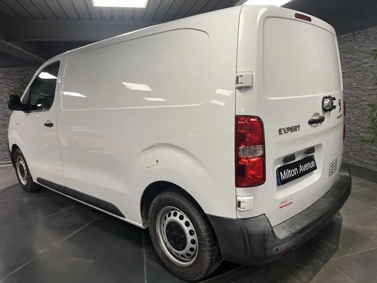 Vue 3/4 arrière droite d'un Peugeot Expert Fourgon blanc avec boucliers noirs et portes arrière tôlées ouvertes à 180°.