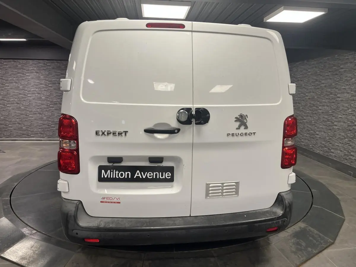Vue arrière d'un Peugeot Expert Fourgon blanc avec portes battantes et bouclier noir dans un showroom.