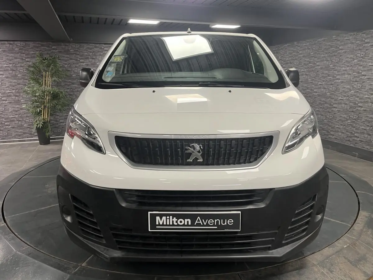 Vue frontale d'un Peugeot Expert Fourgon blanc avec boucliers noirs et calandre noire en intérieur showroom.