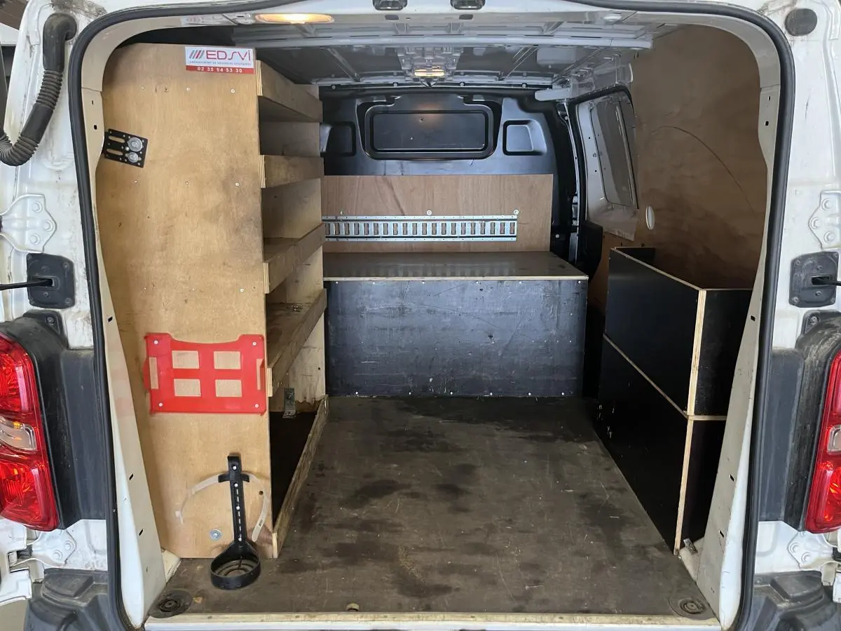 Vue arrière du Peugeot Expert Fourgon blanc 2020 montrant l'intérieur utilitaire avec étagères et plancher bois antidérapant.