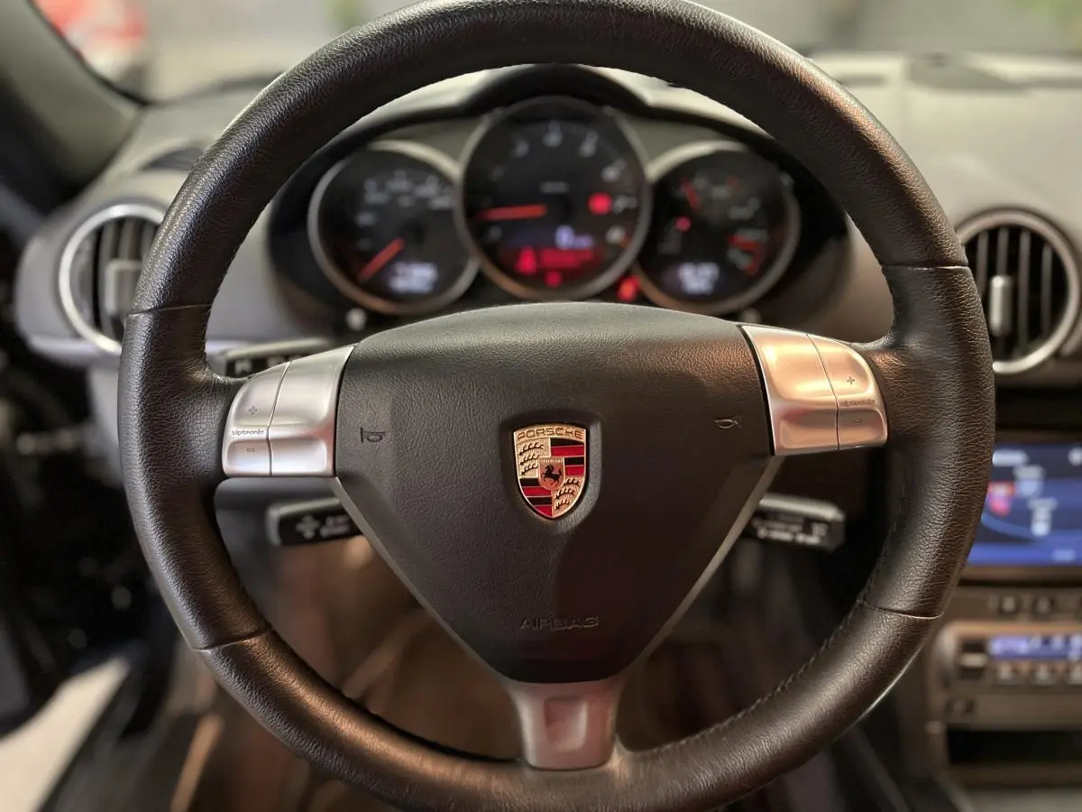 Intérieur de Porsche Cayman 987 noir, vue rapprochée du volant cuir avec commandes Tiptronic et tableau de bord en arrière-plan.