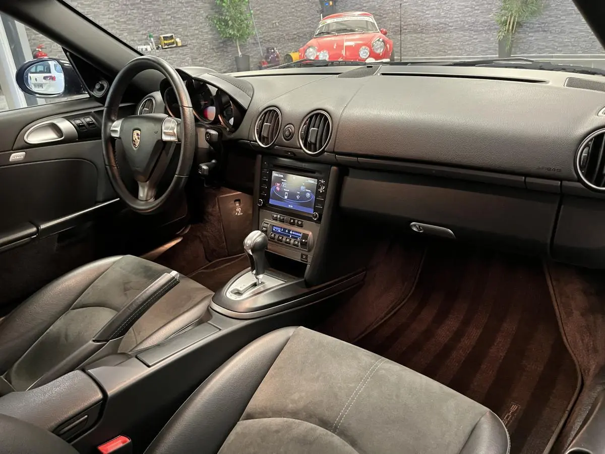 Intérieur noir de Porsche Cayman 987 2.7i 2008 vu côté conducteur avec console centrale et volant Porsche visible.