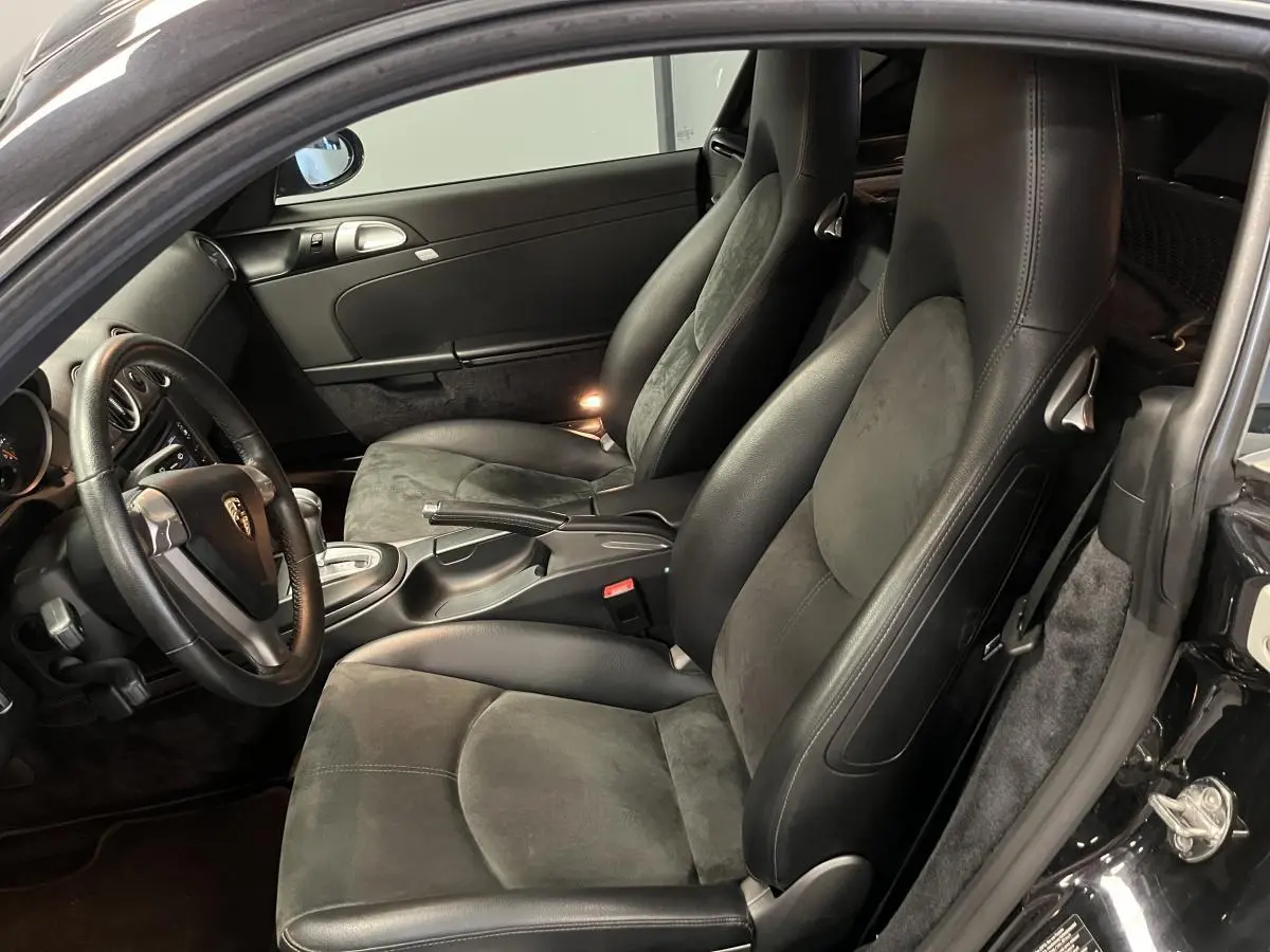 Intérieur noir de Porsche Cayman 987 vu côté gauche, avec sièges sport en cuir et alcantara, volant 3 branches.