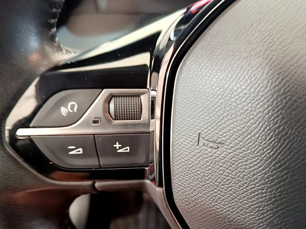 Gros plan sur les commandes gauche du volant cuir noir de la Peugeot 208 PureTech blanche, version 2020.