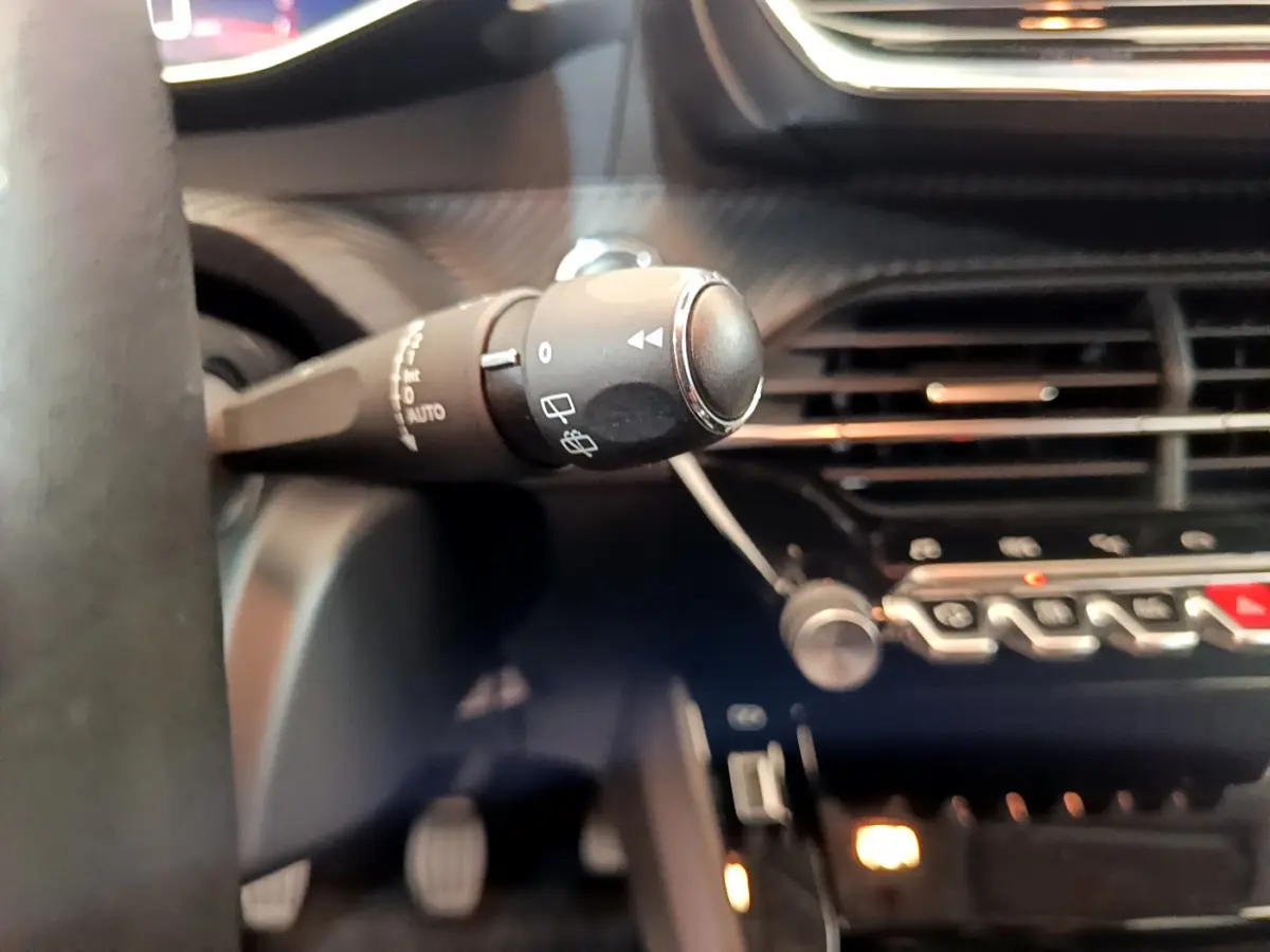 Gros plan sur la commande d’essuie-glace à gauche du volant dans l’habitacle sombre d’une Peugeot 208 blanche 2020.