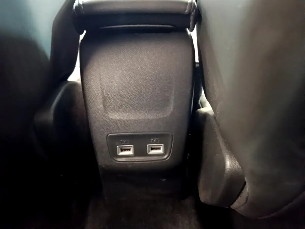 Vue rapprochée des ports USB arrière entre les sièges noirs de la Peugeot 208 PureTech 100 S&S Allure Business blanche.