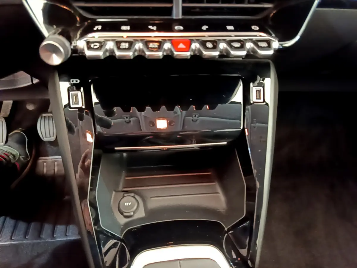 Vue rapprochée de la console centrale noire du Peugeot 208 blanc, avec commandes et prise 12V visibles.