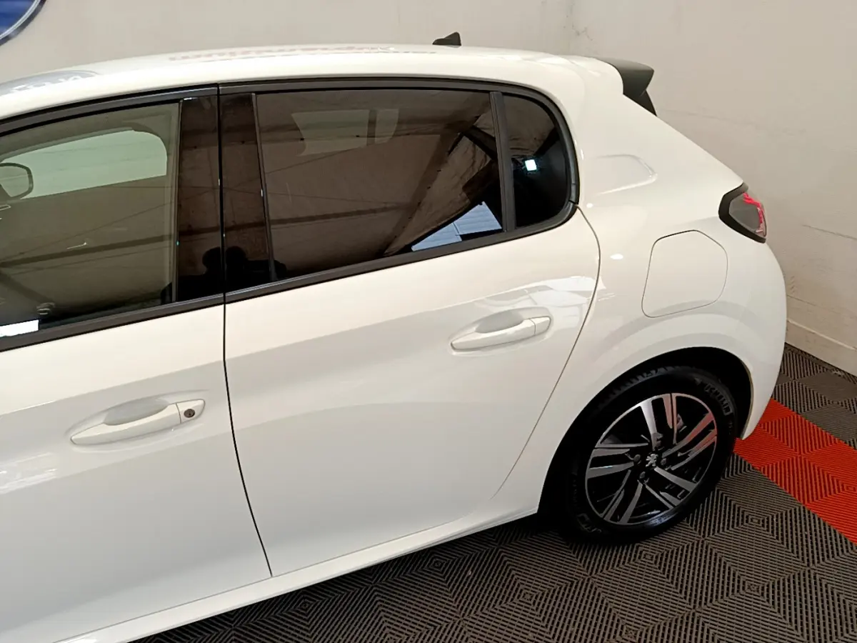 Vue latérale côté gauche d'une Peugeot 208 blanche, mettant en valeur les vitres teintées et les jantes alliage modernes.