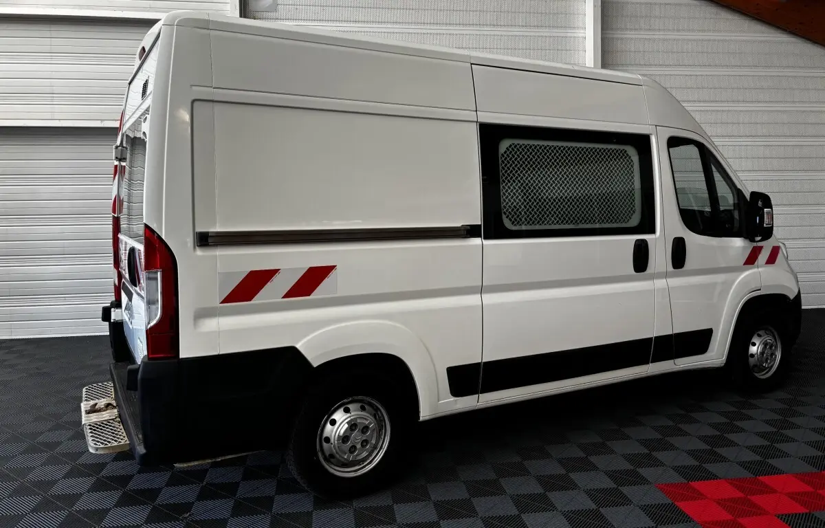 Vue latérale droite d’un utilitaire blanc Citroën Jumper 35 L2H2 avec marquages réfléchissants rouges et grille de protection sur la fenêtre.