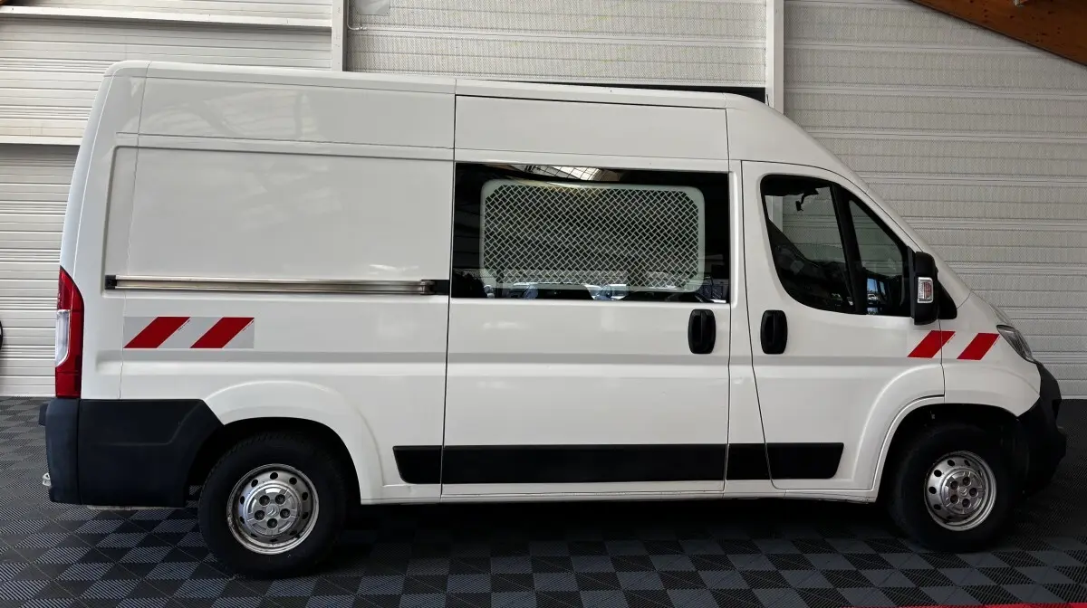 Vue latérale droite d’un utilitaire blanc Citroën Jumper 35 L2H2 avec marquages rouges et grille de protection sur la fenêtre.
