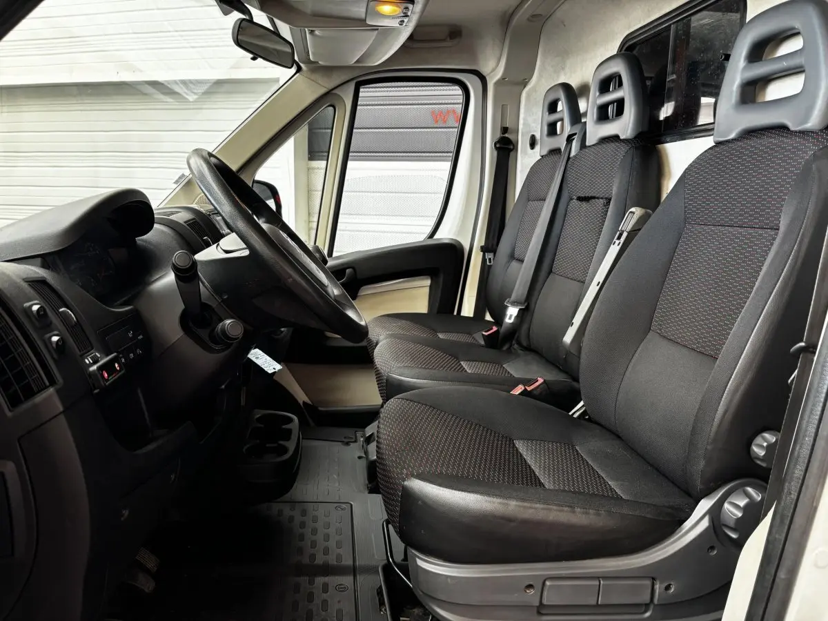 Vue intérieure côté conducteur du Citroën Jumper blanc, montrant le volant multifonctions et les trois sièges avant en tissu noir.