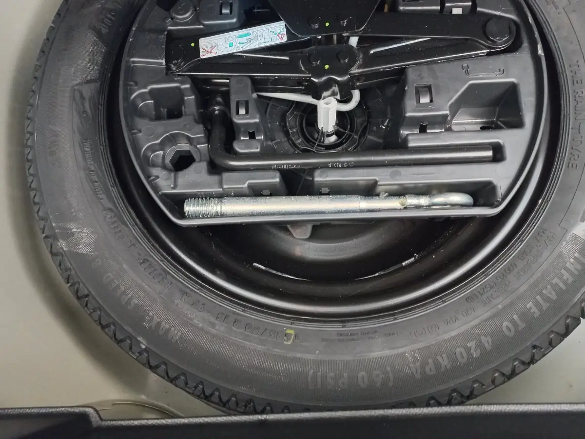 Gros plan sur la roue de secours noire et les outils de bord du coffre d'une Peugeot 208 blanche.