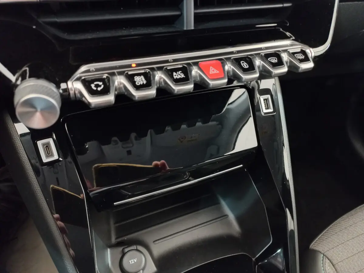 Vue rapprochée de la console centrale noire brillante du Peugeot 208 PureTech 100 Allure avec boutons et ports USB visibles.