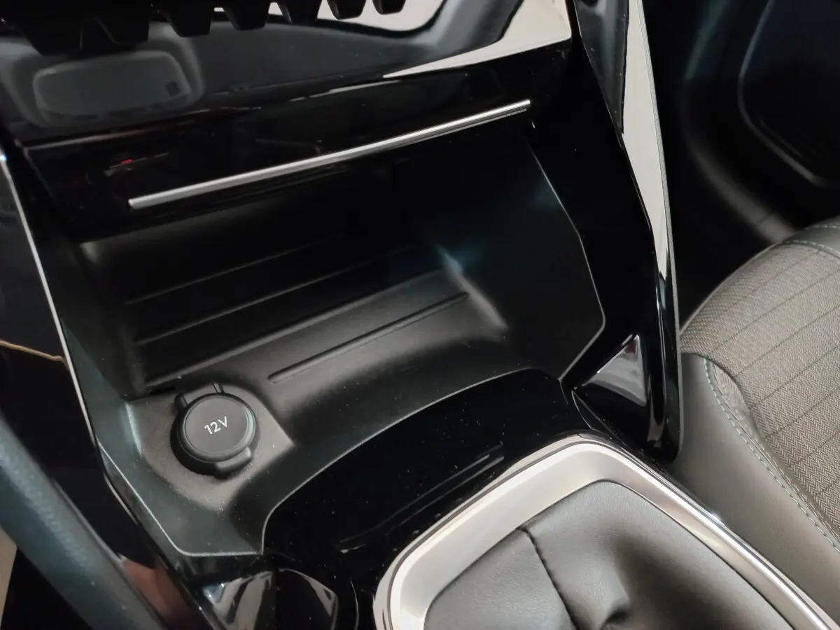 Prise 12V et rangement central noir brillant dans l'habitacle côté droit de la Peugeot 208 blanche PureTech 100 S&S Allure 2021.