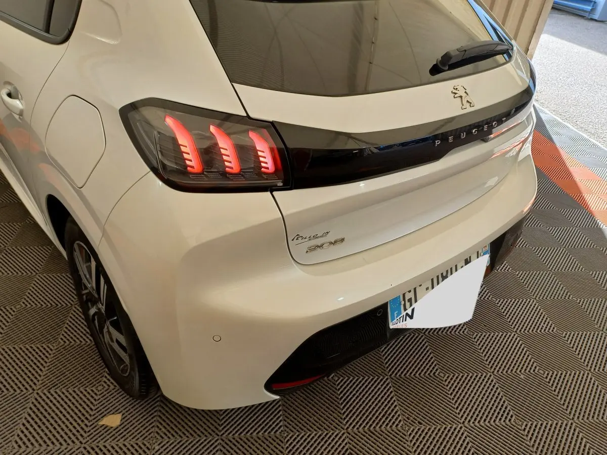 Vue 3/4 arrière droite d'une Peugeot 208 blanche avec feux arrière LED et logo Peugeot sur hayon noir brillant
