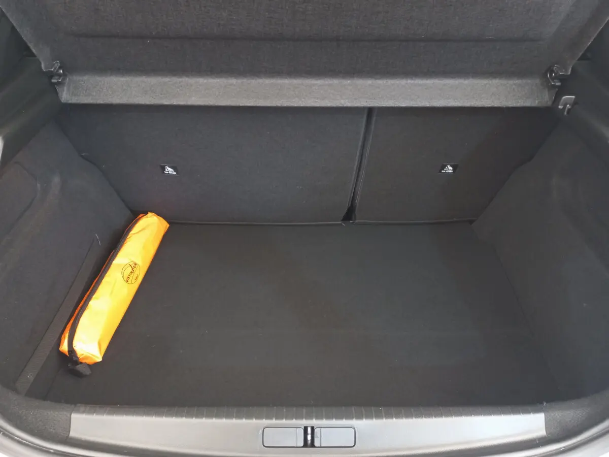 Coffre ouvert de Peugeot 208 blanc, vue intérieure montrant un rangement spacieux avec une trousse de sécurité orange sur la gauche.