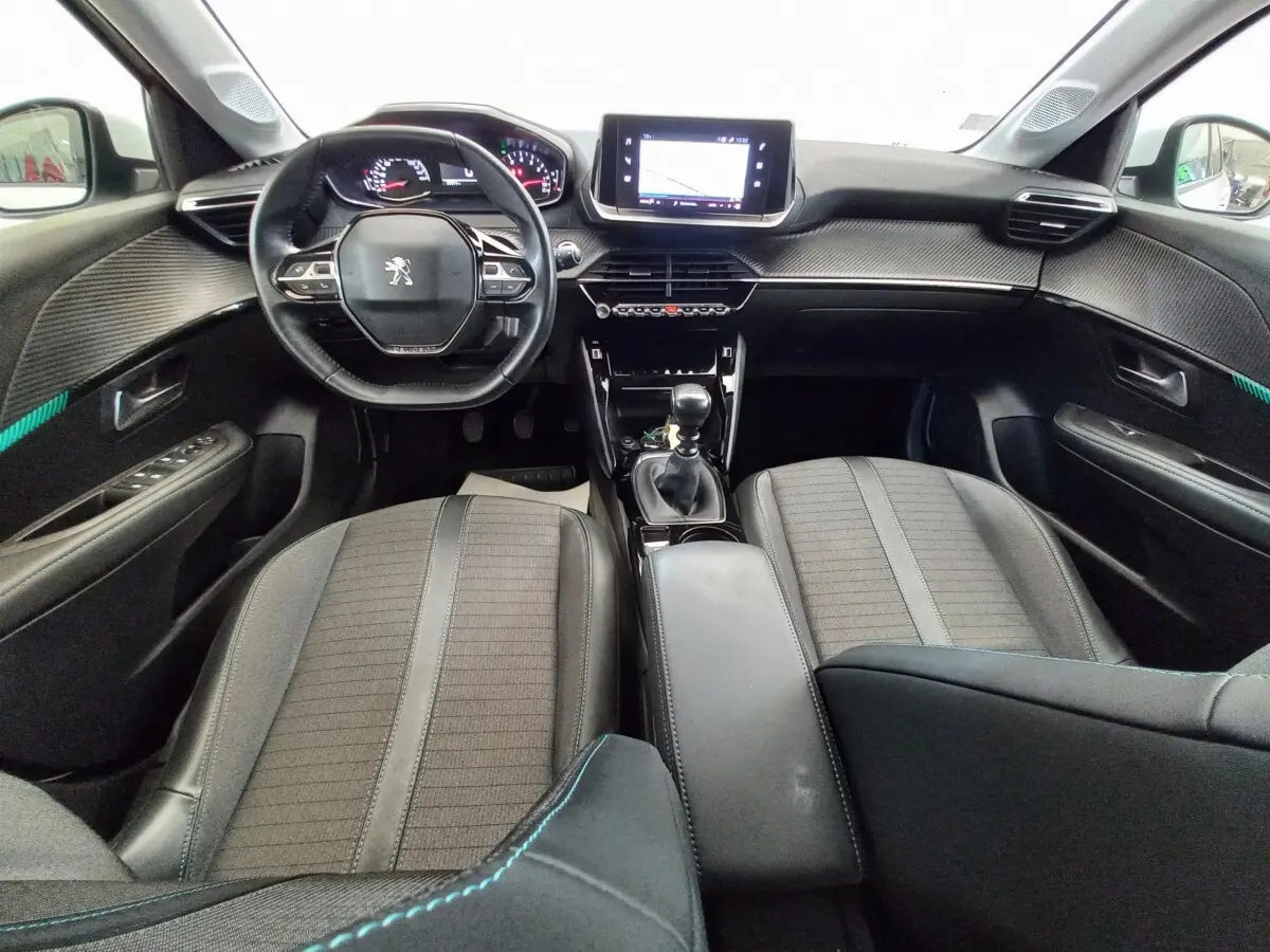 Intérieur noir de la Peugeot 208 PureTech 100 S&S Allure 2021, vue avant centrée sur le tableau de bord et volant cuir.