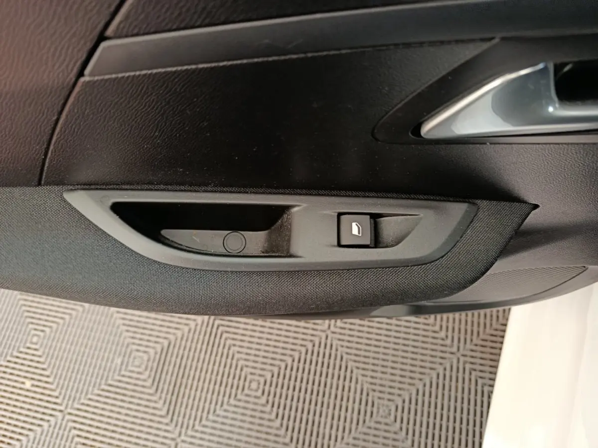 Détail de la commande de lève-vitre électrique sur la porte côté conducteur d'une Peugeot 208 électrique blanche.