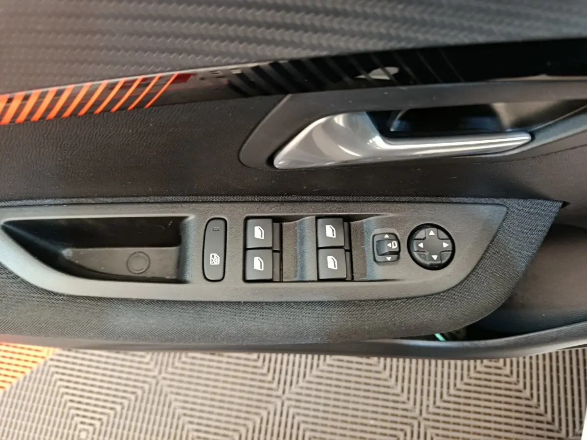 Gros plan sur la commande des vitres électriques et réglages des rétroviseurs côté conducteur d’une Peugeot 208 blanche.