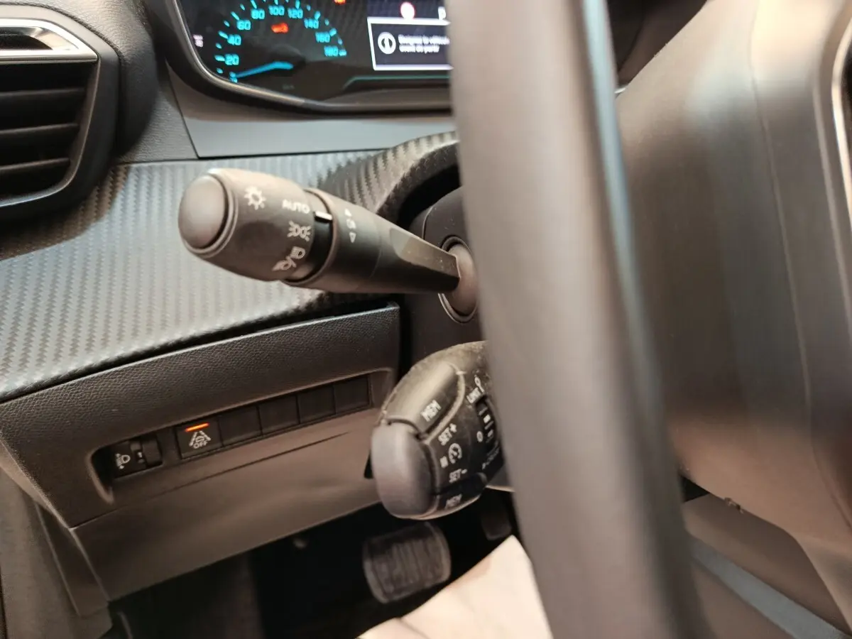 Gros plan sur le volant et les commandes de la Peugeot 208 électrique blanche, tableau de bord digital en arrière-plan.