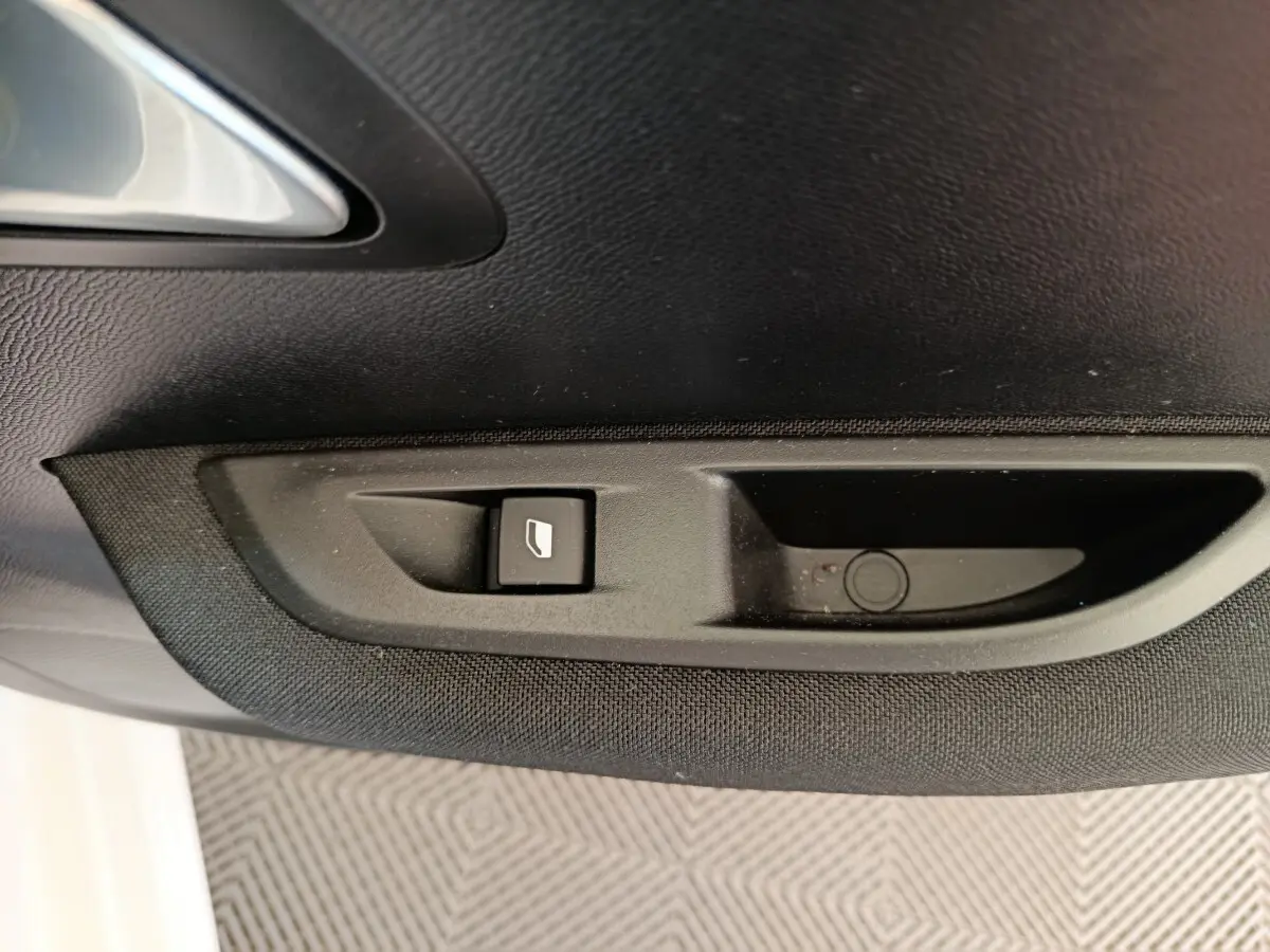 Bouton de commande de vitre électrique sur la porte intérieure côté gauche d'une Peugeot 208 électrique blanche.