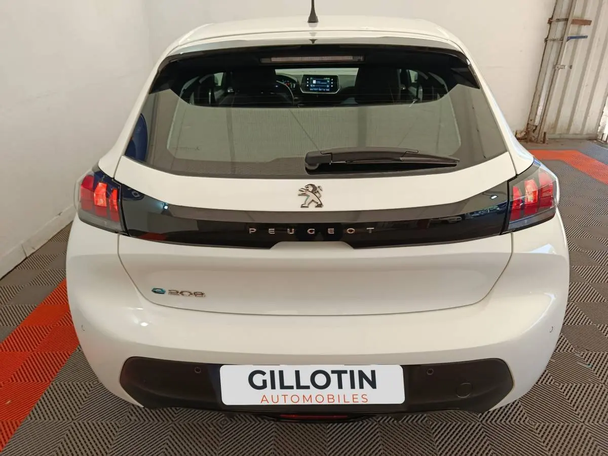 Vue arrière d'une Peugeot 208 électrique blanche avec bande noire et feux arrière LED distinctifs.