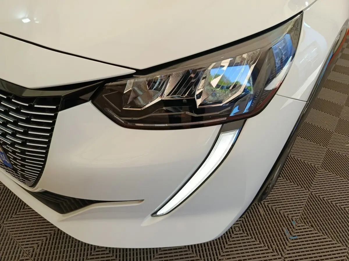 Gros plan sur le phare avant droit blanc d'une Peugeot 208 électrique avec signature lumineuse LED en forme de griffes.